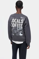 Buzo oversize gris oscuro con cuello redondo, hombros caídos y pequeño texto estampado en el pecho. Presenta puños y bajo con ribete acanalado.