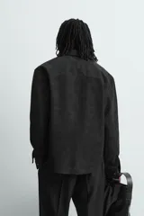 Sobrecamisa de corte relajado confeccionada en tejido efecto piel color marrón oscuro. Presenta cuello solapa, cierre frontal con botones metálicos, mangas largas con puños abotonados y dos bolsillos de plastrón con solapa en el pecho.