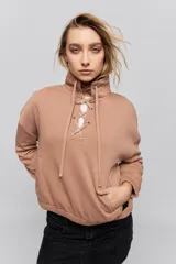 Buzo de calce relajado color tostado, con cuello alto y detalle de cordones entrelazados con ojales metálicos en el frente. Posee bolsillos laterales ocultos y puños y ruedo elastizados.