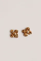 Aros tipo studs con diseño de flor de cuatro pétalos en metal dorado con centro texturizado.