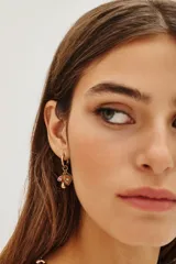 Aro tipo argolla dorada con dos dijes colgantes: un hongo rojo con blanco y un corazón dorado con una piedra brillante en el centro.