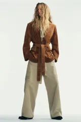 Chaqueta tipo blazer confeccionada en piel de ante, con cuello de solapa, hombreras y manga larga. Presenta cierre frontal con botones, bolsillos delanteros con solapa y un cinturón lazada del mismo material para ajustar a la cintura.