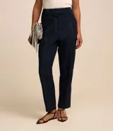 Pantalón de vestir negro, estilo carrot (holgado en cadera y ajustado en tobillo), de cintura alta con trabillas y cierre tradicional. Presenta recortes verticales con costura aparente en el frente.