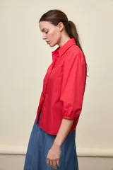 Camisa de algodón blanca con cuello camisero, frente abotonado y mangas abullonadas de corte relajado.