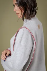 Buzo de lana color beige con cuello redondo y costuras decorativas bordadas en color naranja a lo largo de los laterales y puños. Presenta un diseño holgado y mangas largas.