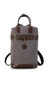 Mochila matera de diseño vertical, confeccionada en tela canvas marrón con detalles y refuerzos en cuero sintético oscuro. Cuenta con doble asa superior de mano, correas traseras regulables, cierre metálico frontal y bolsillo posterior.