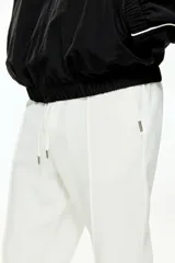 Pantalón tipo jogger de corte sastrero, color blanco, confeccionado en tejido de punto de peso medio. Presenta pliegue cosido frontal, cintura elástica con cordón de ajuste, bolsillos laterales y bolsillo trasero insertado.