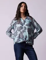 Blusa celeste con estampado de flores grises, de gasa, con cuello con solapa y escote en V, abertura central con botones, bolsillo aplicado y terminación anudada.