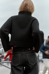 Chaqueta estilo bomber de punto color negro, con cuello subido, manga larga y cierre frontal cruzado con botones ocultos a presión. Presenta bolsillos delanteros de vivo.