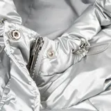 Campera puffer plateada, acolchada y liviana, con capucha ajustable, cuello alto, cierre y botones a presión.