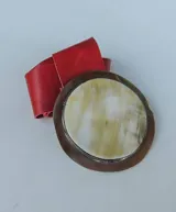 Cinturón con hebilla circular de guampa y engarce en alpaca, con tira de cuero rojo.