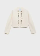 Chaqueta de corte recto y diseño estructurado en color crudo, con cuello redondo y manga larga. Presenta una abertura frontal sin cierre, decorada con ojales metálicos plateados a lo largo de los bordes. Confeccionada en tejido mezcla de algodón con forro interior.