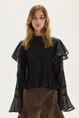 Blusa de manga larga confeccionada en ramio, con diseño de tablas verticales en el frente y la espalda. Presenta cuello alto, cierre frontal con botones y mangas con volados en los hombros y puños acampanados.