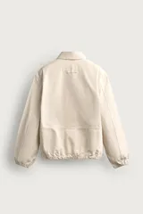 Cazadora de algodón color beige con efecto lavado, corte relaxed fit, cuello solapa y cierre frontal con cremallera. Cuenta con bolsillos frontales tipo canguro, puños y bajo elásticos, y aplicaciones de parches bordados a contraste en el delantero.