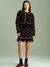 Cardigan de punto con diseño de jacquard en colores negro, rojo y detalles en blanco y violeta. Presenta cuello redondo, cierre frontal con botones, mangas largas y terminaciones acanaladas en puños y ruedo.