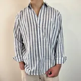 Camisa celeste y blanca a rayas verticales, de manga larga con puños abotonados y cuello clásico.