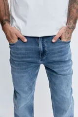Pantalón de jean corte regular, color azul medio con efecto lavado, de tiro medio y cierre frontal con botón y cremallera.