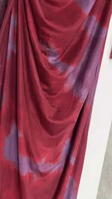 Vestido midi de microtul con diseño drapeado lateral, cuello alto y mangas largas. Presenta un estampado tipo tie-dye en tonos bordó y violeta.