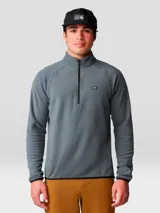 Buzo polar Mountain Hardwear modelo Microchill 1/4 Zip, color gris, con cuello alto, cierre frontal parcial de un cuarto y mangas raglán. Presenta detalles en color negro en los bordes del cuello, puños y ruedo, además de un pequeño logo bordado en el pecho.