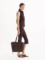 Bolso tipo tote de cuero color tostado con doble asa de hombro, detalles de hebillas metálicas en el frente y cierres laterales decorativos.