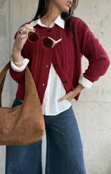 Cardigan de punto con textura trenzada en color bordó, con cuello redondo y cierre frontal mediante botones tipo alamar. Presenta mangas largas con puños acanalados y un corte clásico.