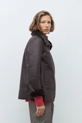 Chaqueta de eco cuero color chocolate con interior y cuello forrados en piel sintética al tono. Presenta cierre frontal completo, bolsillos laterales y diseño de corte recto.