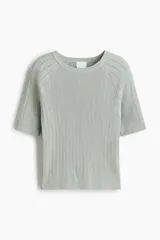 Remera de punto acanalado gris claro, de ajuste entallado con mangas raglán cortas y cuello redondo. Presenta detalles en pointelle y remates acanalados en escote, mangas y bajo.