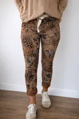 Pantalón de mujer con estampado animal print en tonos marrones y negros, de corte ajustado y largo hasta el tobillo. Incluye un cinturón de tela a rayas blancas y marrones.