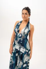 Vestido largo con escote halter profundo y diseño sin mangas. Presenta un estampado difuminado en tonos azules, celestes, blancos y grises, con corte ajustado en el torso y una falda larga con vuelo.
