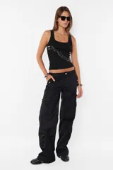 Pantalón cargo negro de corte recto y tiro bajo, con recortes y múltiples bolsillos laterales y traseros con tapa y botón a presión. Cierre frontal con cremallera de nylon y botón personalizado.