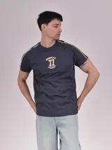 Remera gris oscuro con cuello redondo, mangas cortas con rayas blancas y amarillas en los hombros, y estampado frontal con la palabra "Brooklyn" y el número 77 en amarillo.