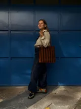 Cartera tipo tote de cuero con diseño de franjas verticales multicolores en tonos tierra, rojo y azul. Cuenta con correas trenzadas de cuero y cierre superior.