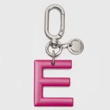 Llavero o charm de letra A en color fucsia, con mosquetón metálico y dije circular pequeño con la marca grabada.
