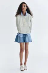 Buzo de cuello redondo en color beige, con hombros caídos y ajuste holgado. Presenta una letra A grande en relieve con textura afelpada en el centro del pecho y un pequeño bordado debajo. Cuenta con puños y cintura acanalados.