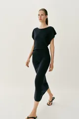 Vestido largo de punto color negro, con cuello barco, manga corta y frunces laterales en la cintura.