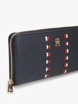 Billetera rectangular con cierre de cremallera perimetral, confeccionada en poliuretano con acabado granulado. Presenta un diseño en color azul marino con dos franjas verticales decorativas formadas por pequeñas piezas en rojo y blanco, y el monograma TH metálico en el centro.