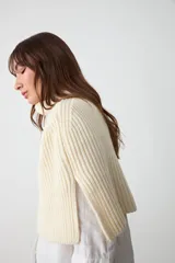 Capita de punto color crudo, con cuello alto vuelto y diseño amplio y corto.