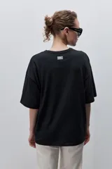 Remera negra de silueta amplia y calce relajado, con cuello redondo, mangas cortas con hombros caídos y estampa botánica en líneas blancas en el frente.