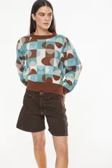 Sweater de tejido de punto con diseño geométrico multicolor en tonos marrón, celeste, verde y crudo. Presenta cuello redondo, mangas largas abullonadas y puños y ruedo elásticos en color marrón.