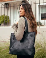 Bolso tipo tote de cuero negro con textura de reptil en la parte superior y base de cuero liso. Cuenta con doble asa de hombro.