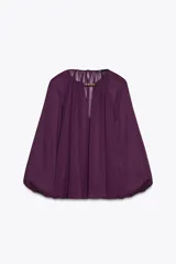 Blusa de tejido semitransparente color violeta, con cuello redondo y detalle de fornitura dorada en el escote. Presenta un diseño de escote en pico, mangas largas abullonadas con puños elásticos y corte holgado.