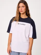 Remera oversize de manga corta marca Rusty, modelo Rocca, en combinación de colores celeste, blanco y detalles en verde. Presenta estampado frontal con el logo de la marca y diseño de bloques de color.