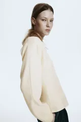 Remera de punto fino suave color beige, con escote en V, cintura entallada y mangas dolman largas.