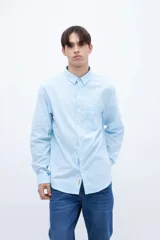 Camisa celeste de algodón, corte regular fit, con cuello solapa clásico, manga larga, bolsillo en el pecho y botones personalizados.