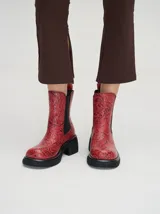 Bota tipo chelsea de cuero vacuno en color rojo con estampado floral grabado en negro. Presenta paneles laterales elásticos, suela de plataforma y taco cuadrado en color negro.