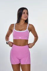 Conjunto deportivo compuesto por un top y un short de tiro alto en color rosa. El top presenta breteles finos blancos, escote redondo y el logo 'bk.' estampado en el centro. El short cuenta con costuras decorativas blancas que resaltan el diseño.