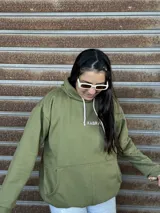 Canguro verde oliva con capucha, cordones en color rosado claro y logo bordado en el pecho. Presenta un bolsillo frontal tipo canguro y diseño holgado.