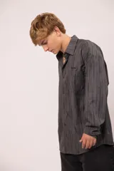 Camisa de manga larga con corte relajado, confeccionada en microfibra con estampado abstracto de líneas verticales en tonos grises. Presenta cuello clásico, cierre frontal con botones, bolsillo en el pecho con el nombre de la marca bordado.