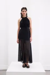 Vestido largo de encaje negro con escote halter, cuerpo ajustado y falda fluida con tajo frontal.