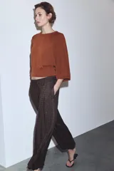 Pantalón de tiro medio con diseño bombacho, confeccionado en tejido con textura plisada y estampado de cuadros vichy en tonos oscuros. Presenta cintura elástica con cordón ajustable y bajos con puños elásticos.